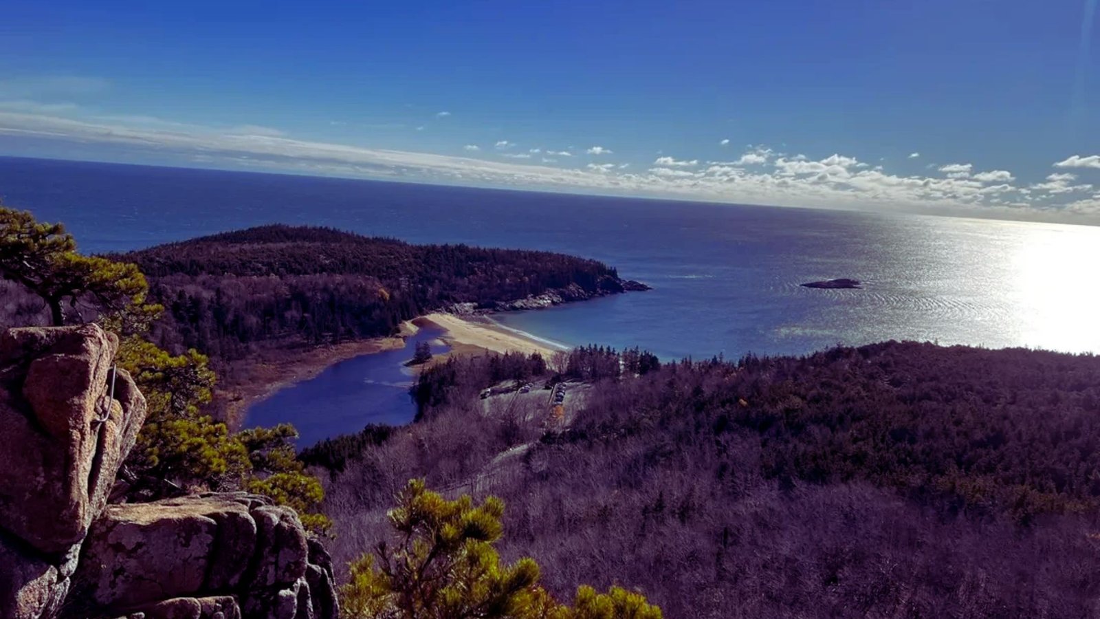 A scenic view of the ocean meeting a rugged rocky cliff under a clear blue sky.