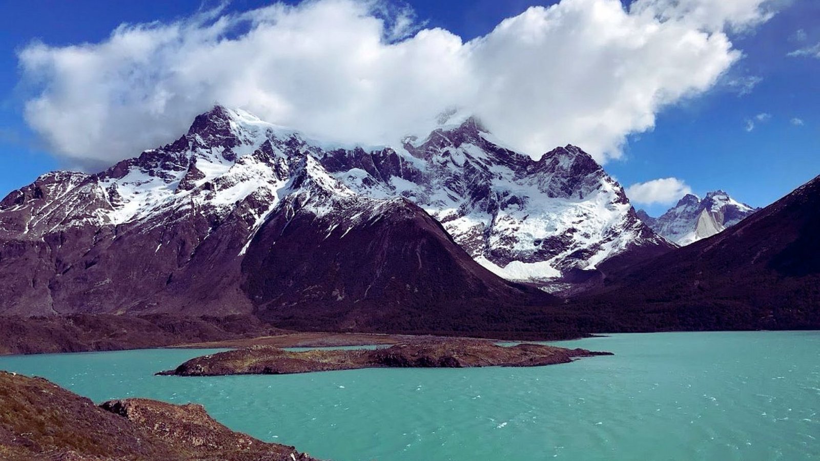 A stunning view of a serene lake surrounded by the majestic mountains of Patagonia, reflecting the clear blue sky.
