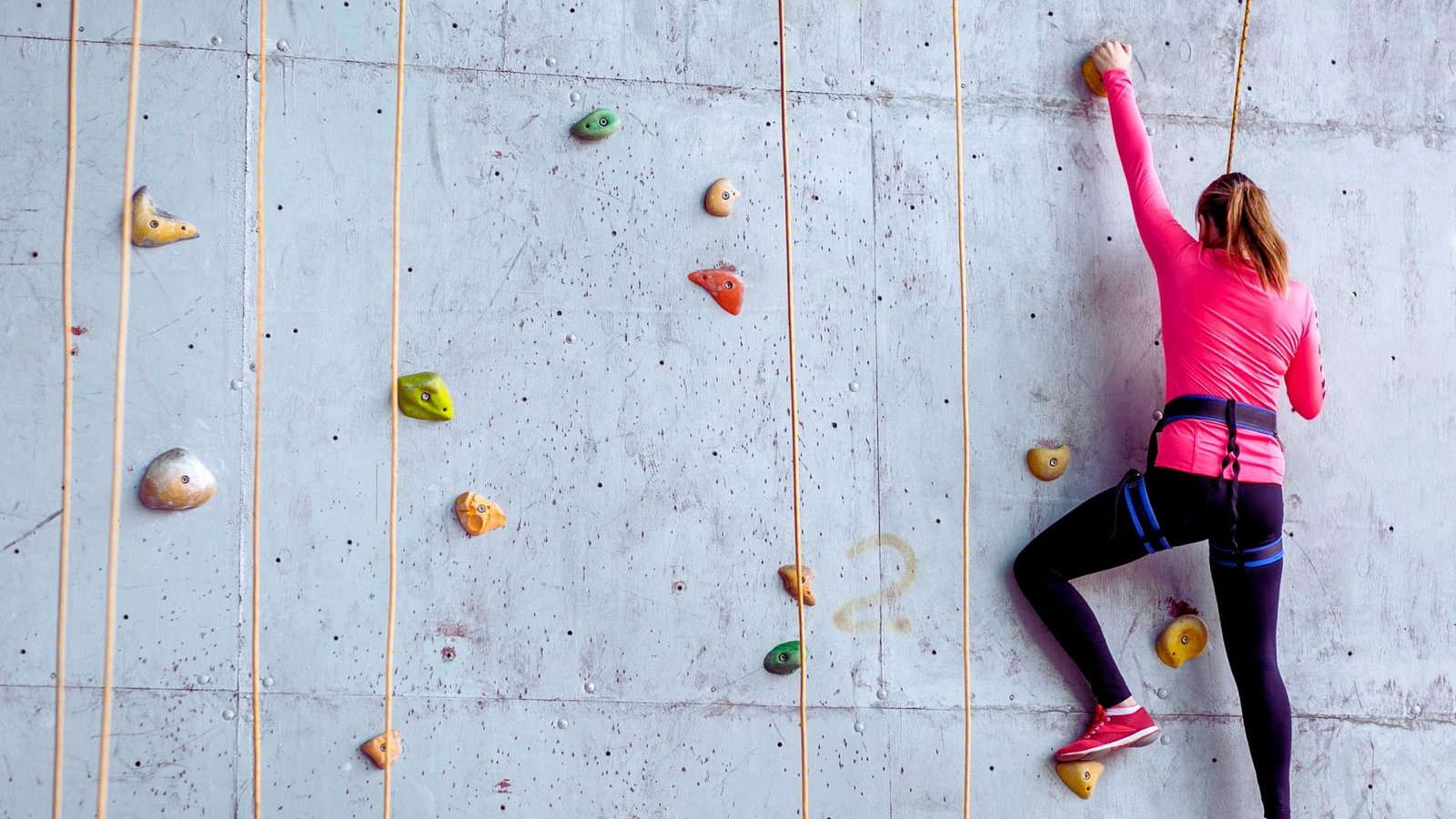 A woman scaling a colorful climbing wall, focused on her ascent with determination and strength.