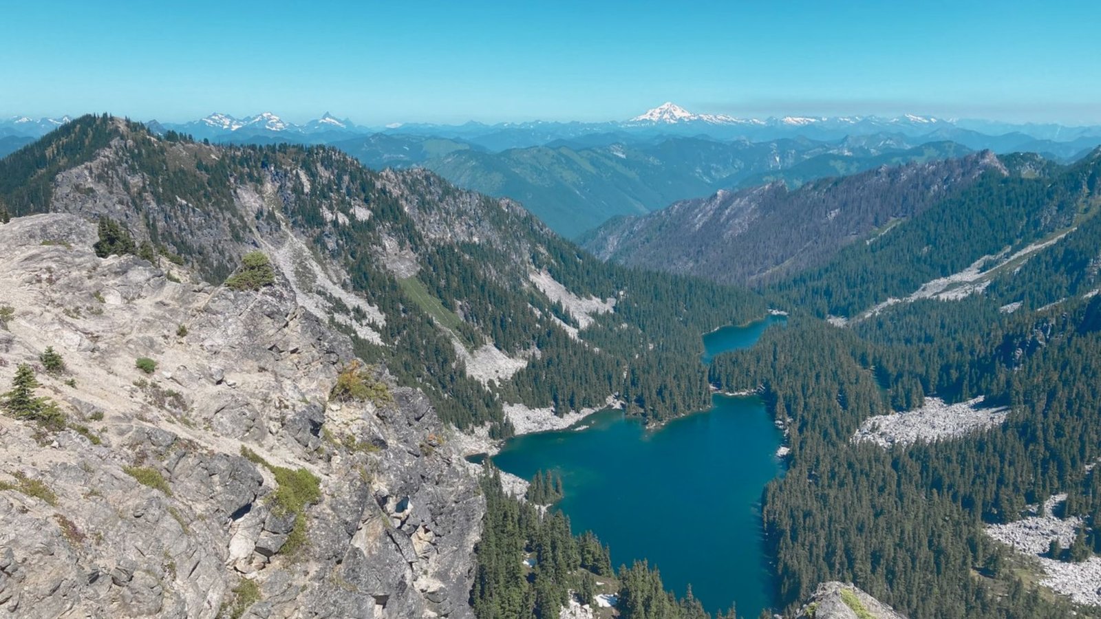  A serene lake nestled among towering mountains and lush green trees under a clear blue sky.
