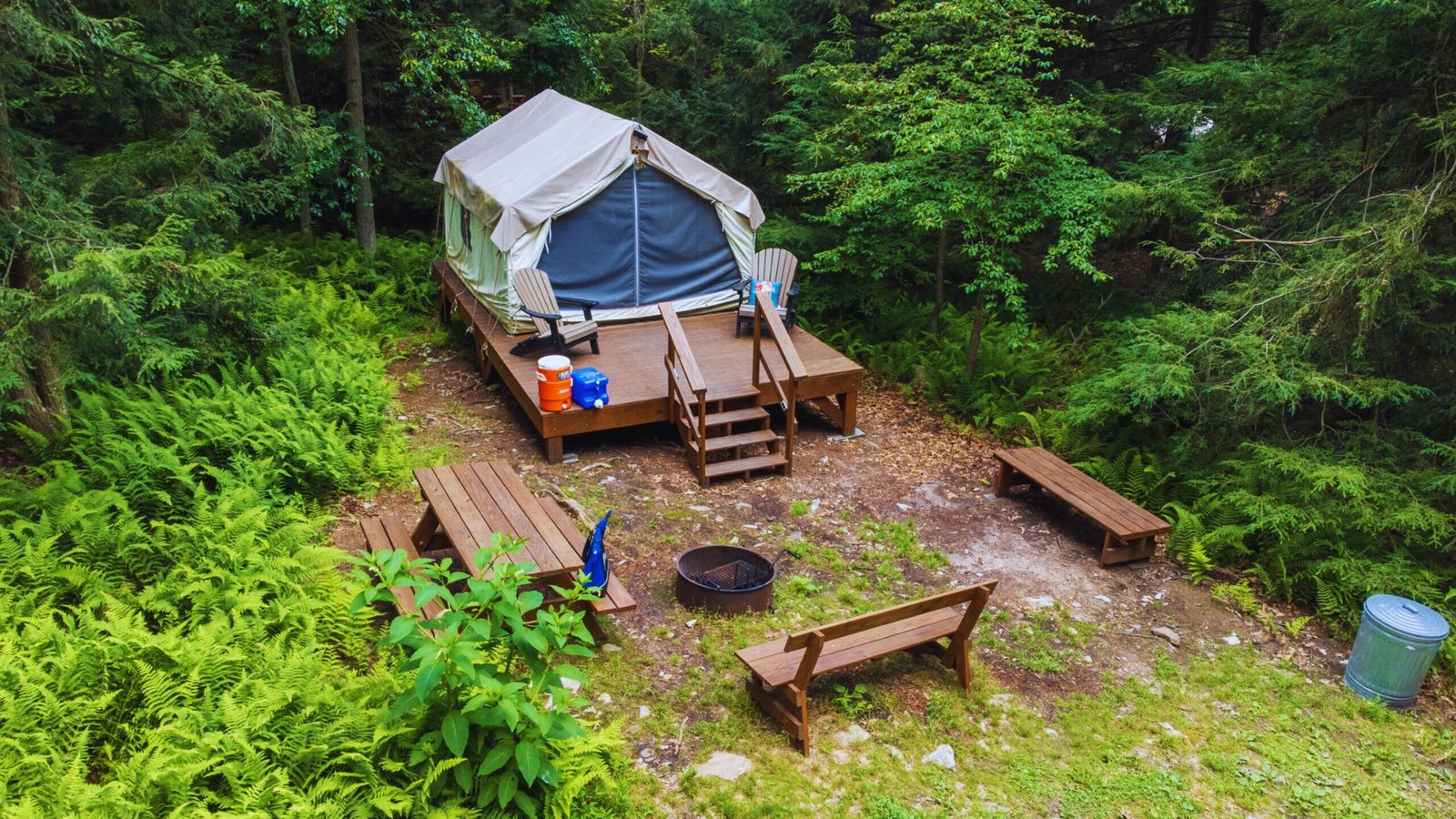  A tent set up in the woods beside a picnic table and benches, ideal for camping and outdoor gatherings.
