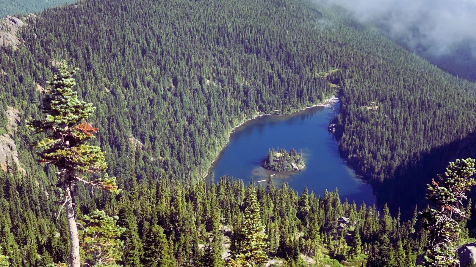 A serene lake bordered by lush trees and majestic mountains under a clear blue sky.