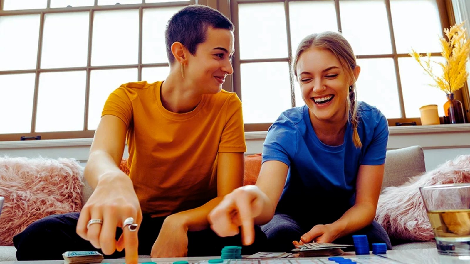 A cozy scene of two individuals playing a board game together on a couch, surrounded by game pieces and snacks.