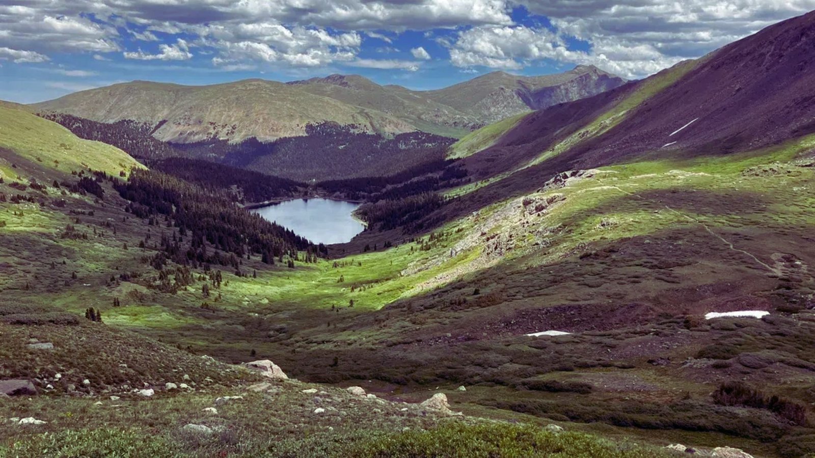 A picturesque mountain valley featuring a serene lake at its center, surrounded by lush greenery and towering peaks.