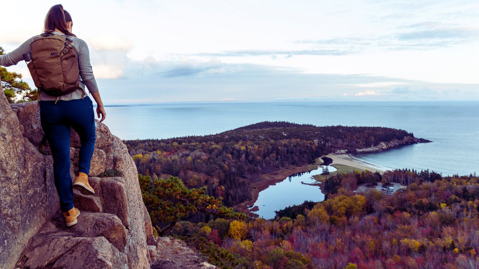 A woman with a backpack overlooks the ocean from a cliff, enjoying the scenic view.