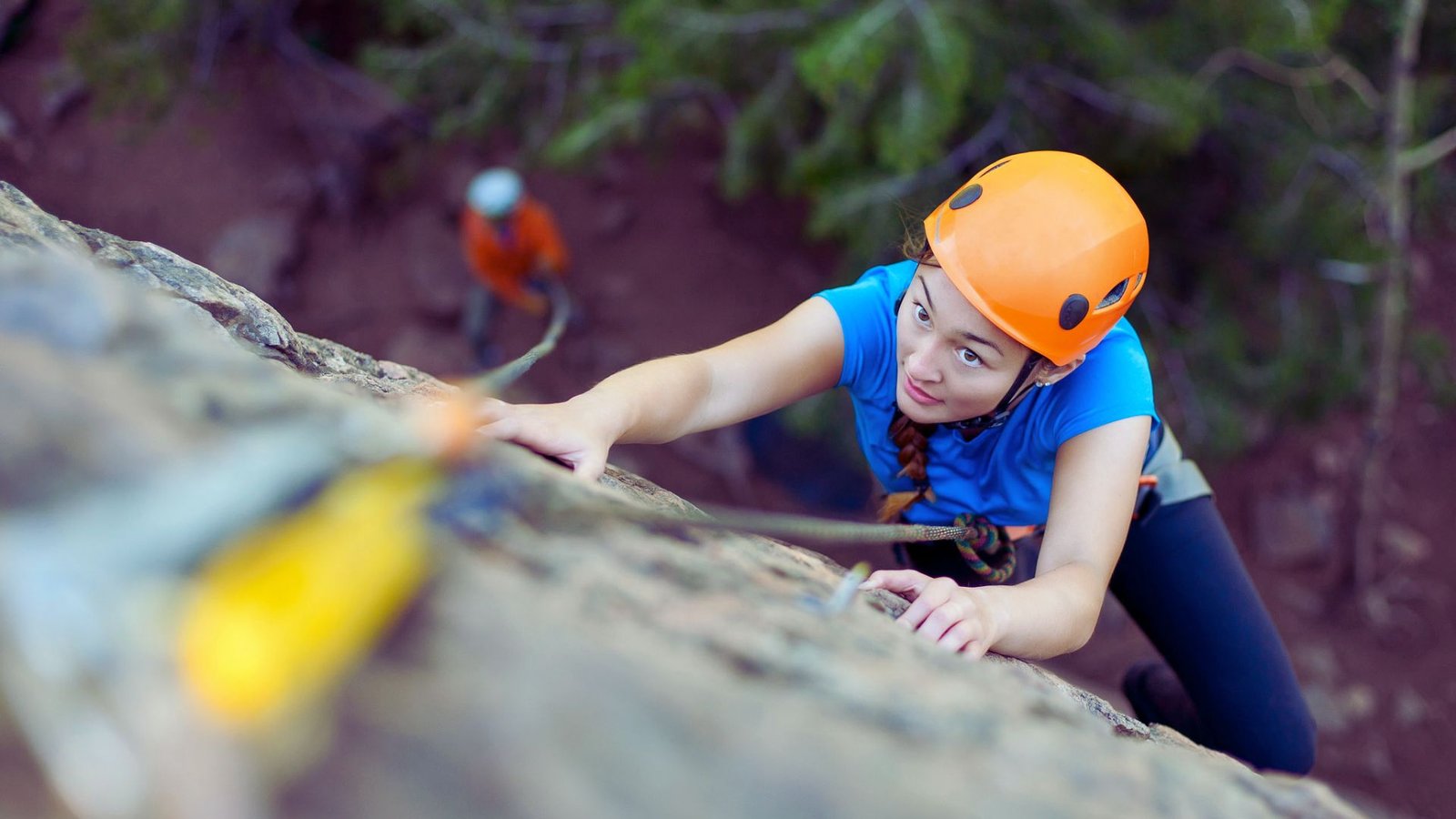 A woman wearing an orange helmet climbs a rocky surface, demonstrating her climbing skills and determination.