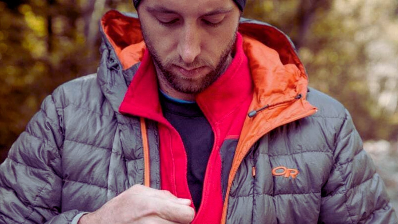  A man wearing a jacket and hat is focused on his phone, appearing engaged in a conversation or activity.