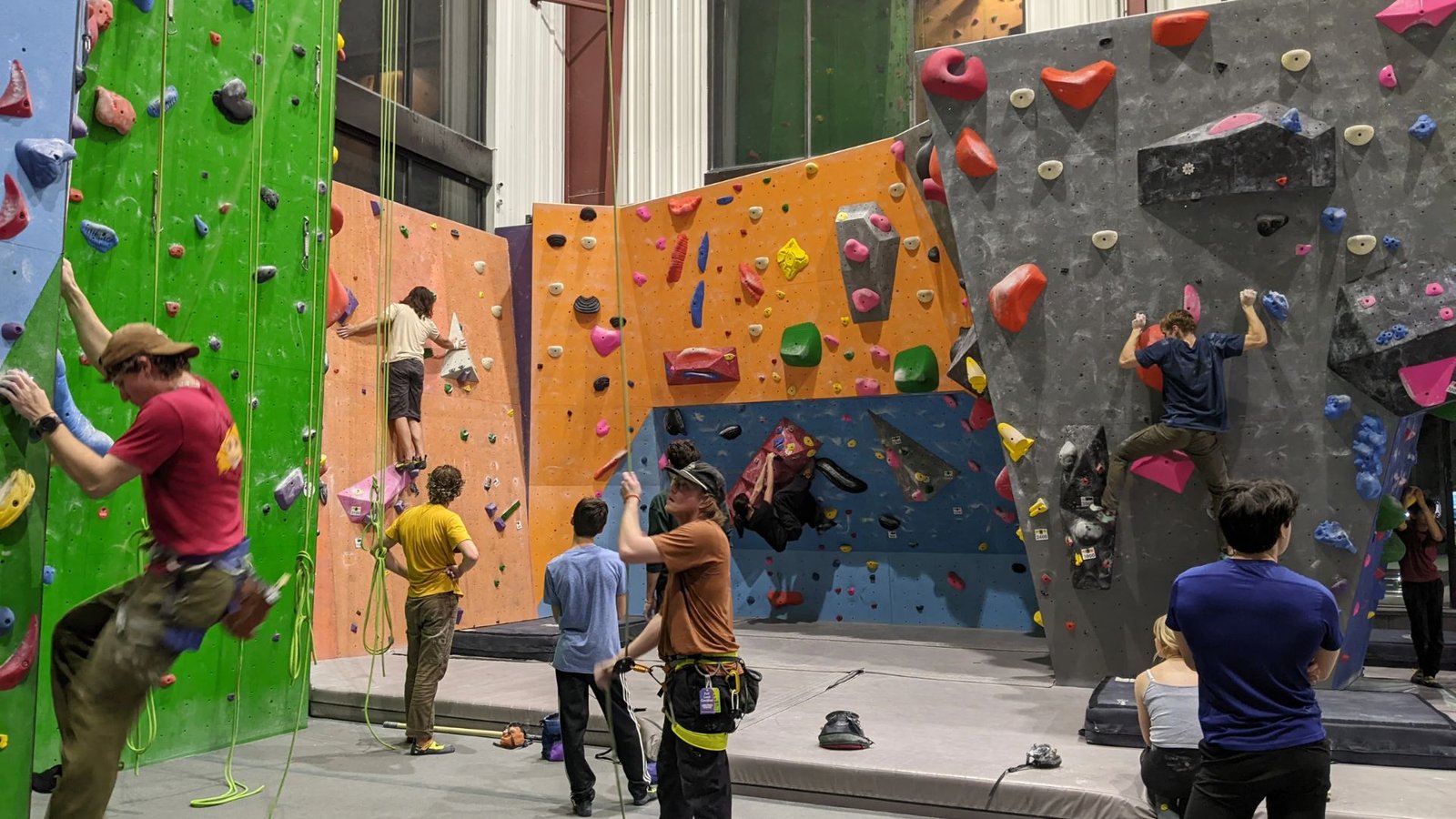 Several climbers of various ages and backgrounds ascend a colorful climbing wall, showcasing teamwork and determination.