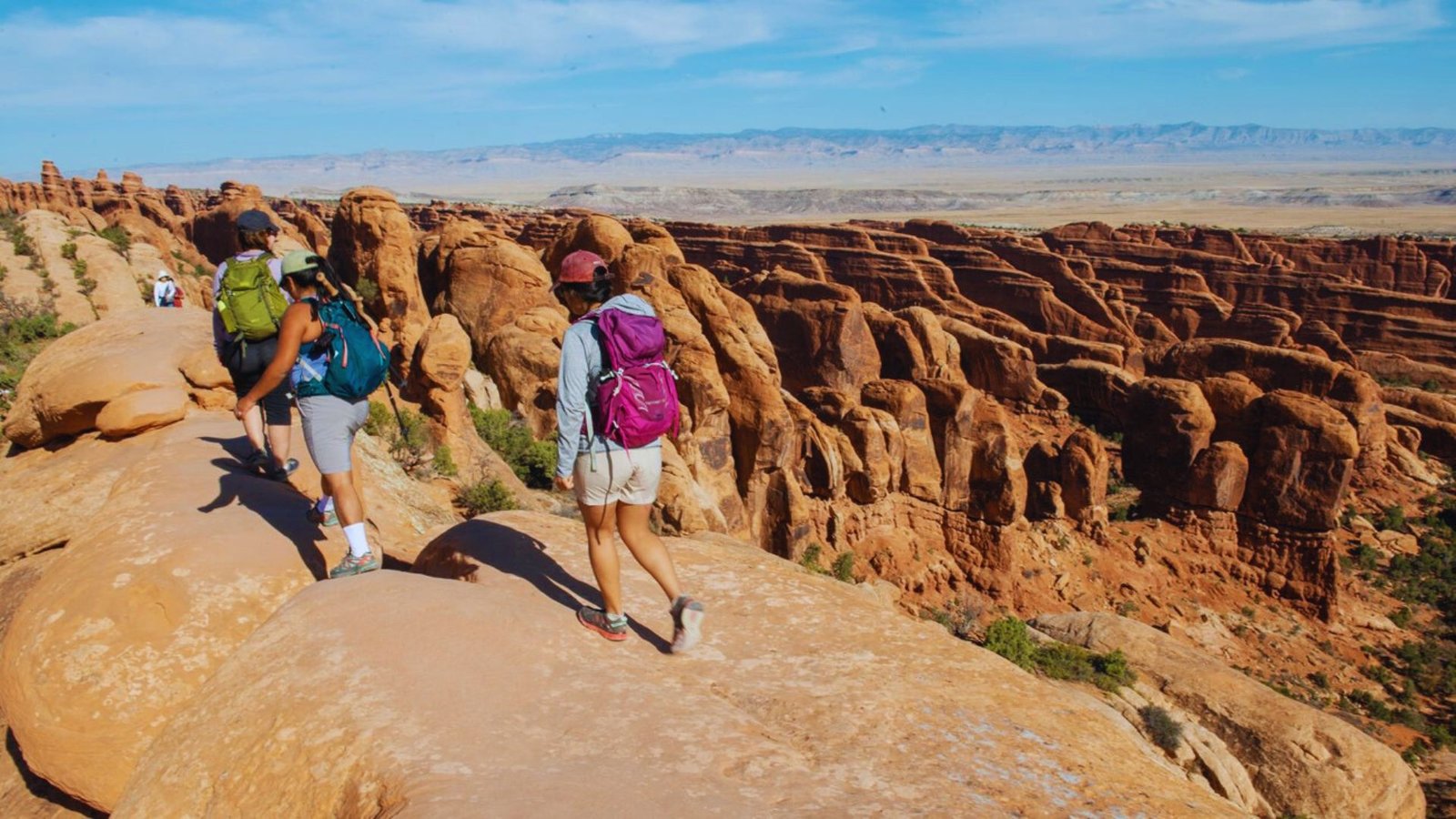 Three hikers with backpacks navigate a rocky trail on the Shi Shi Beach Trail, surrounded by lush greenery.
