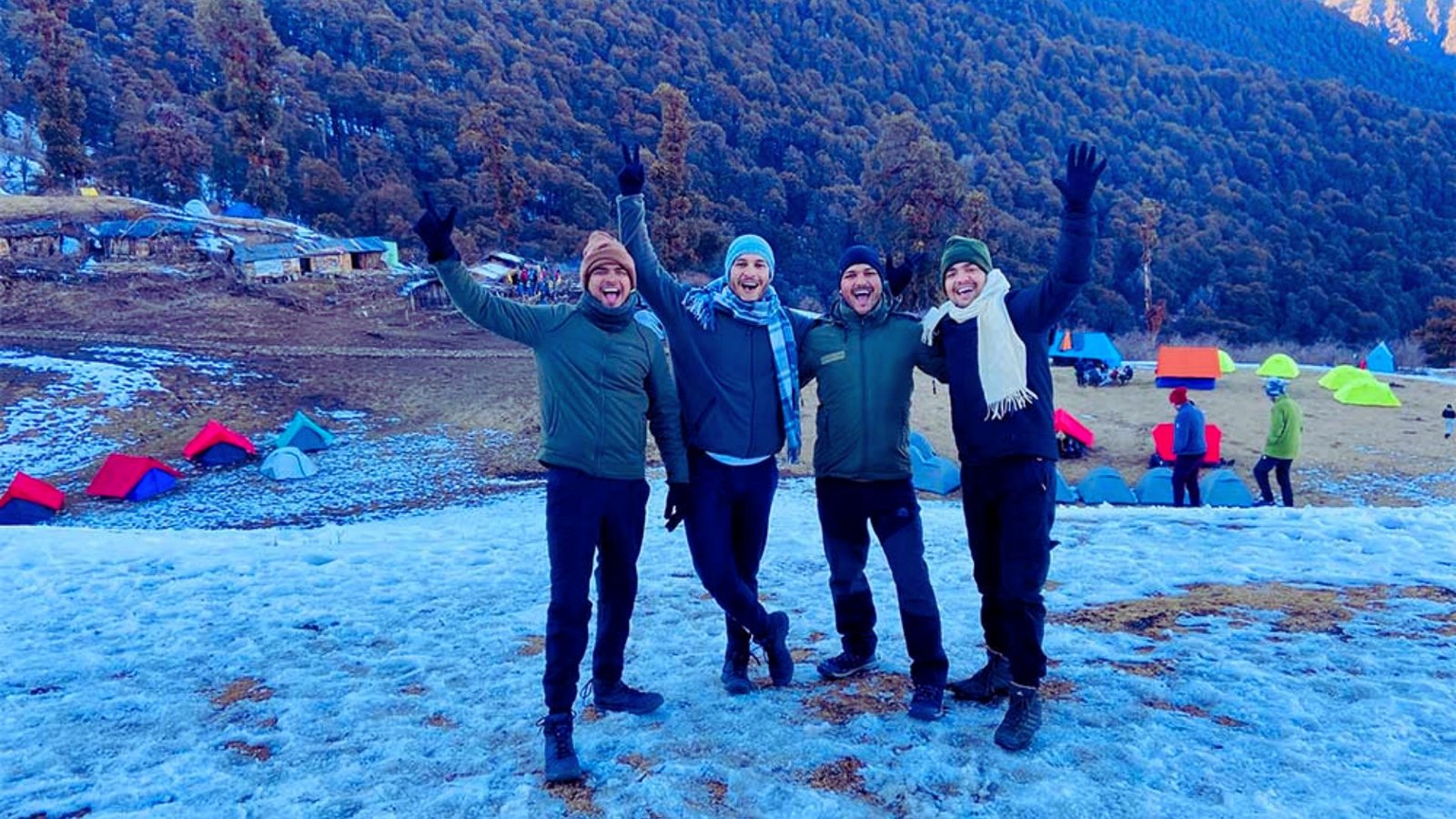 Three people stand triumphantly on a mountain peak, raising their hands in celebration against a clear blue sky.