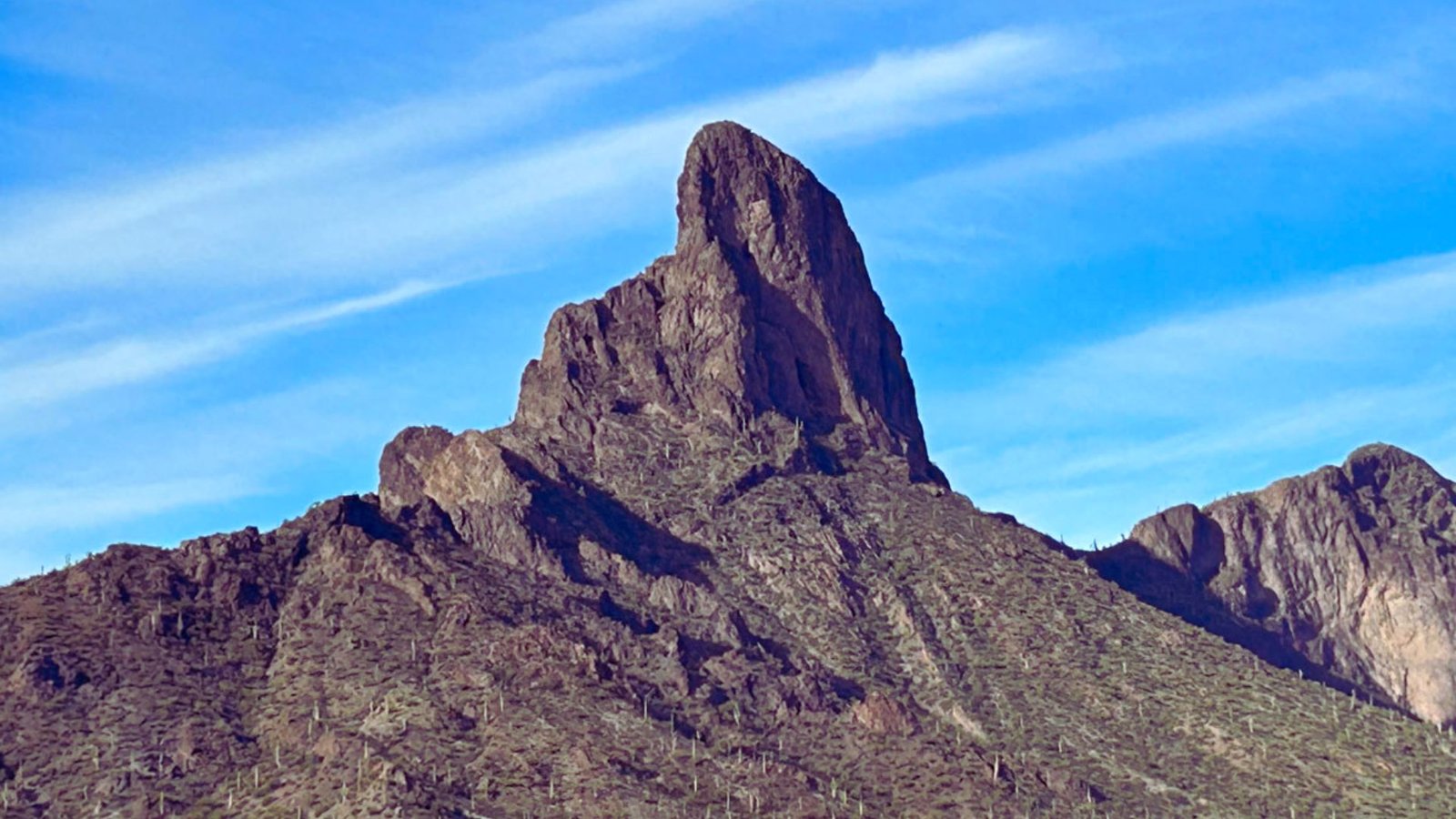 A large mountain topped with a prominent rock formation against a clear blue sky.