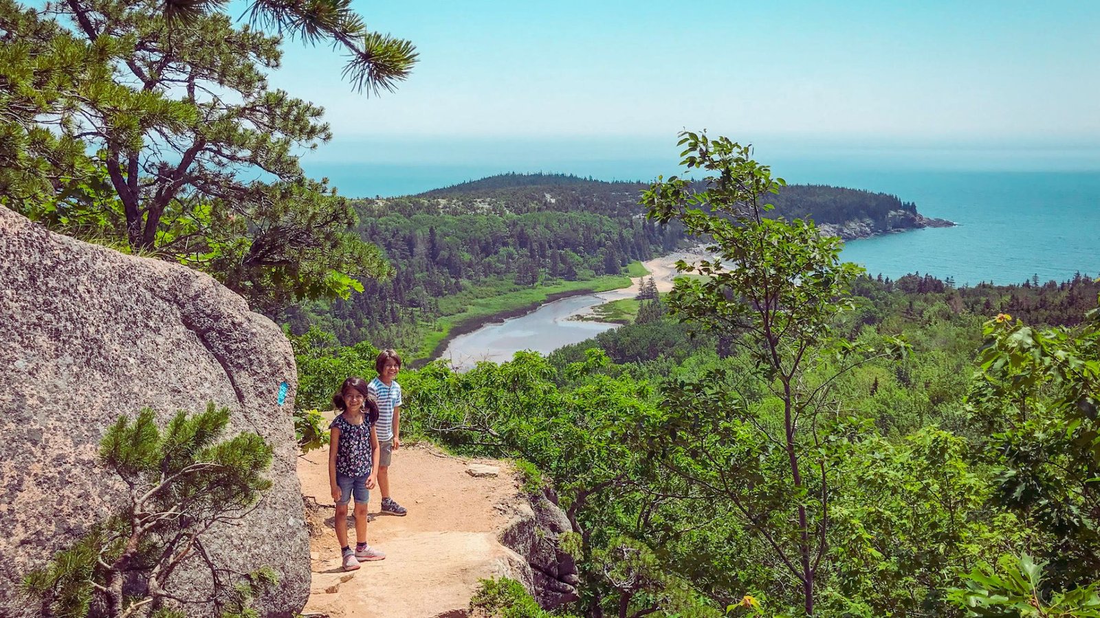 Two individuals stroll on a coastal trail, enjoying the ocean view ahead.