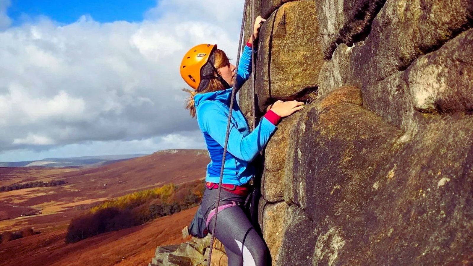 A woman climbs a rock wall, showcasing her strength and determination in an outdoor climbing environment.