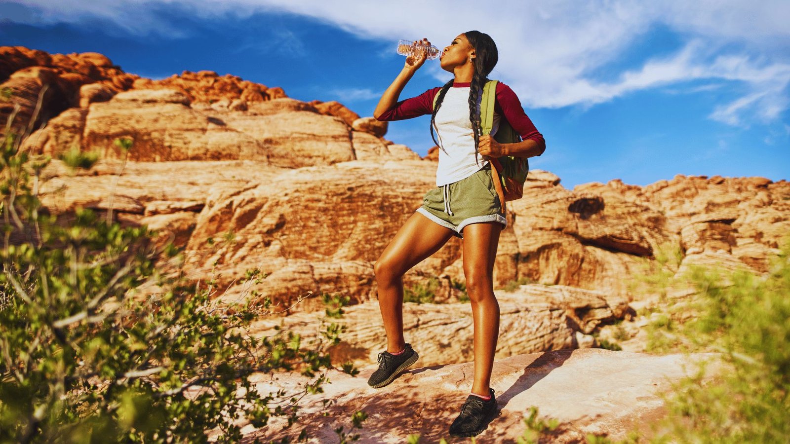 A woman sips water from a bottle on a rocky hiking trail, enjoying the outdoor landscape around her.
