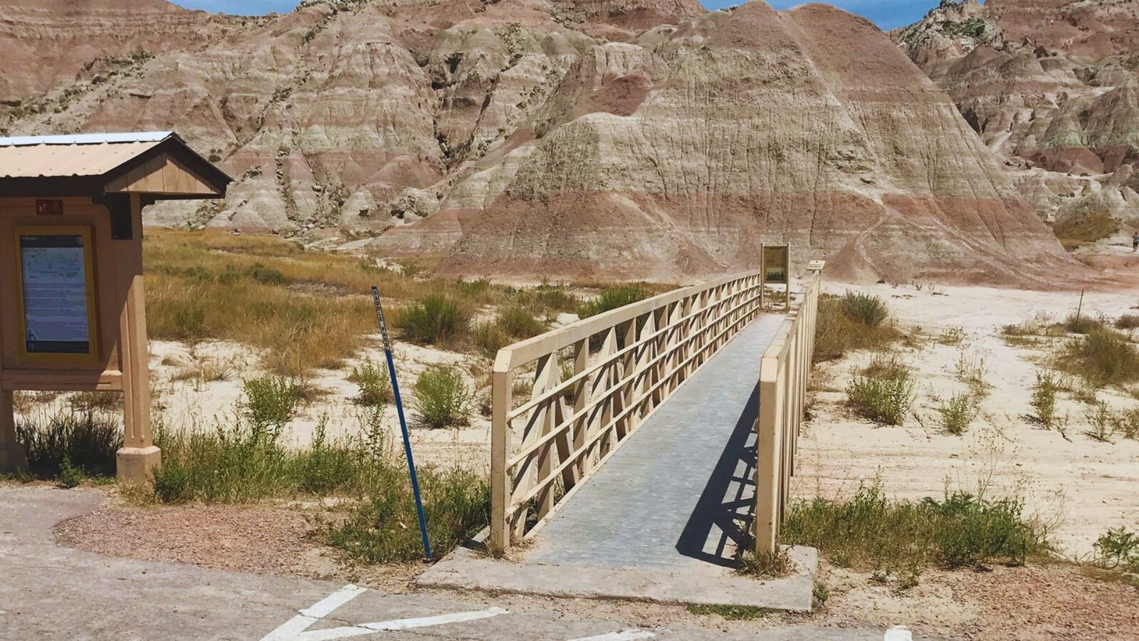 A wooden bridge spans across a vast, arid desert landscape under a clear blue sky.
