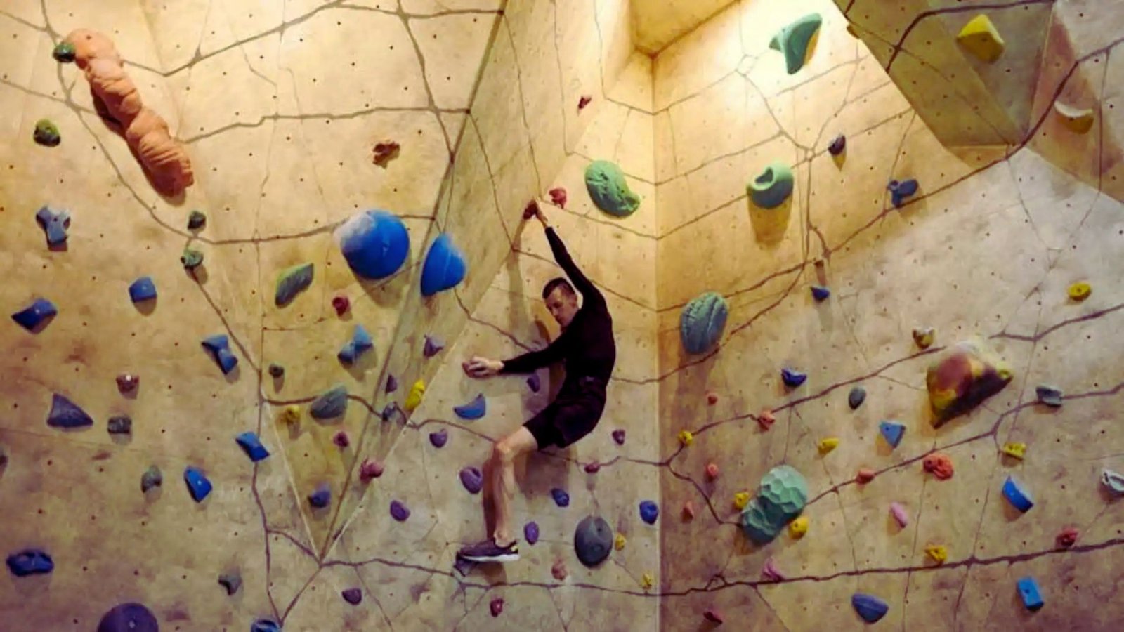 A person climbing a colorful rock wall inside a gym, focused on reaching the next hold.