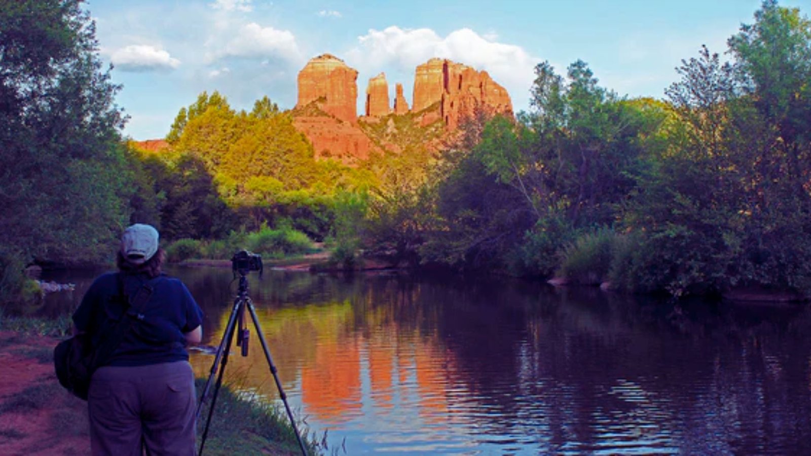 A man photographing a scenic river with mountains in the background, capturing the beauty of nature.