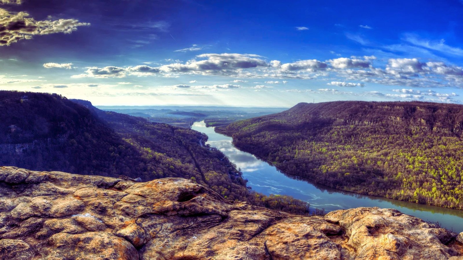 A panoramic view of a river winding through the valley, seen from a mountain top under a clear blue sky.