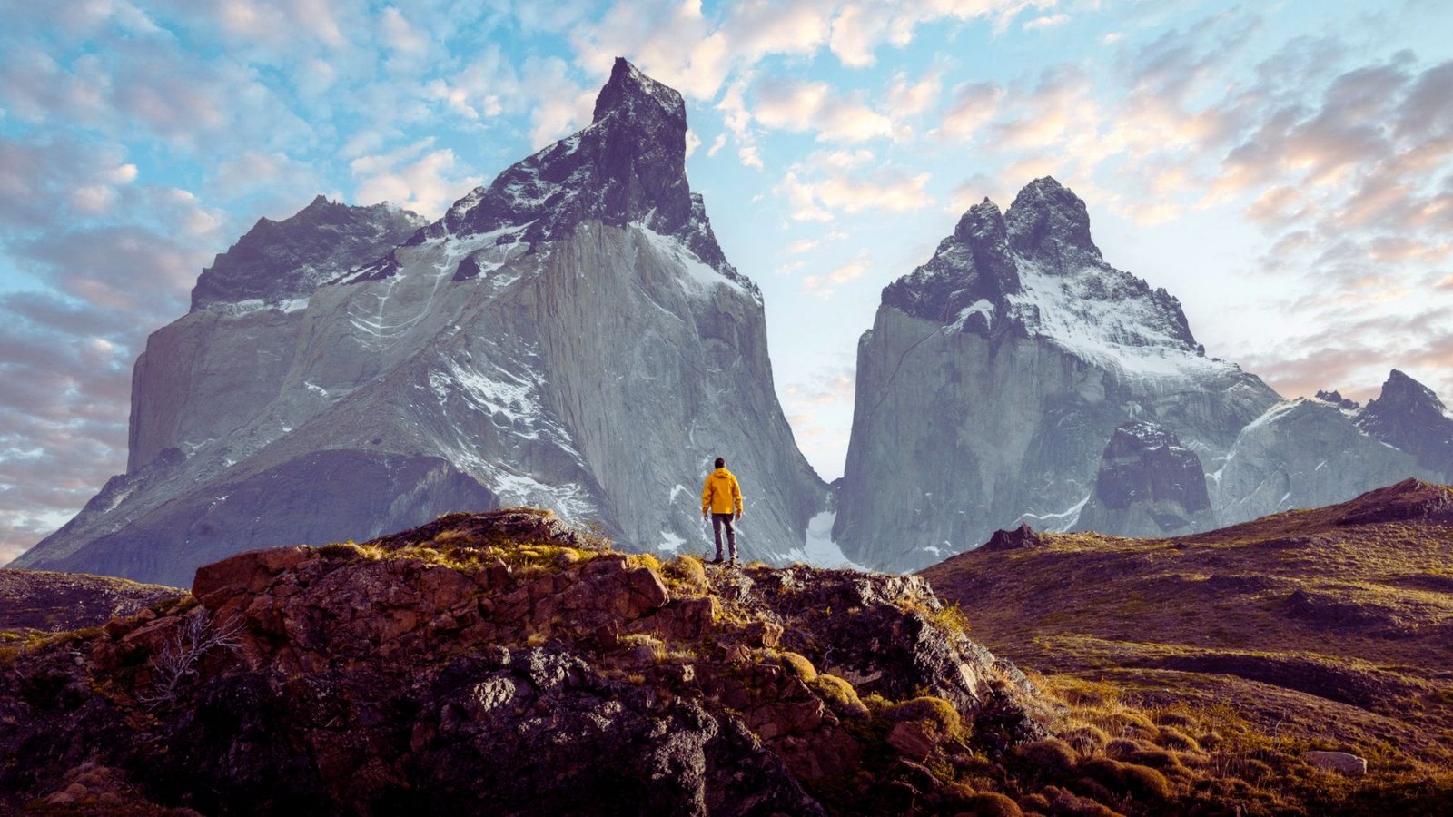 A man stands atop a mountain, gazing at a panoramic view of surrounding peaks and valleys.