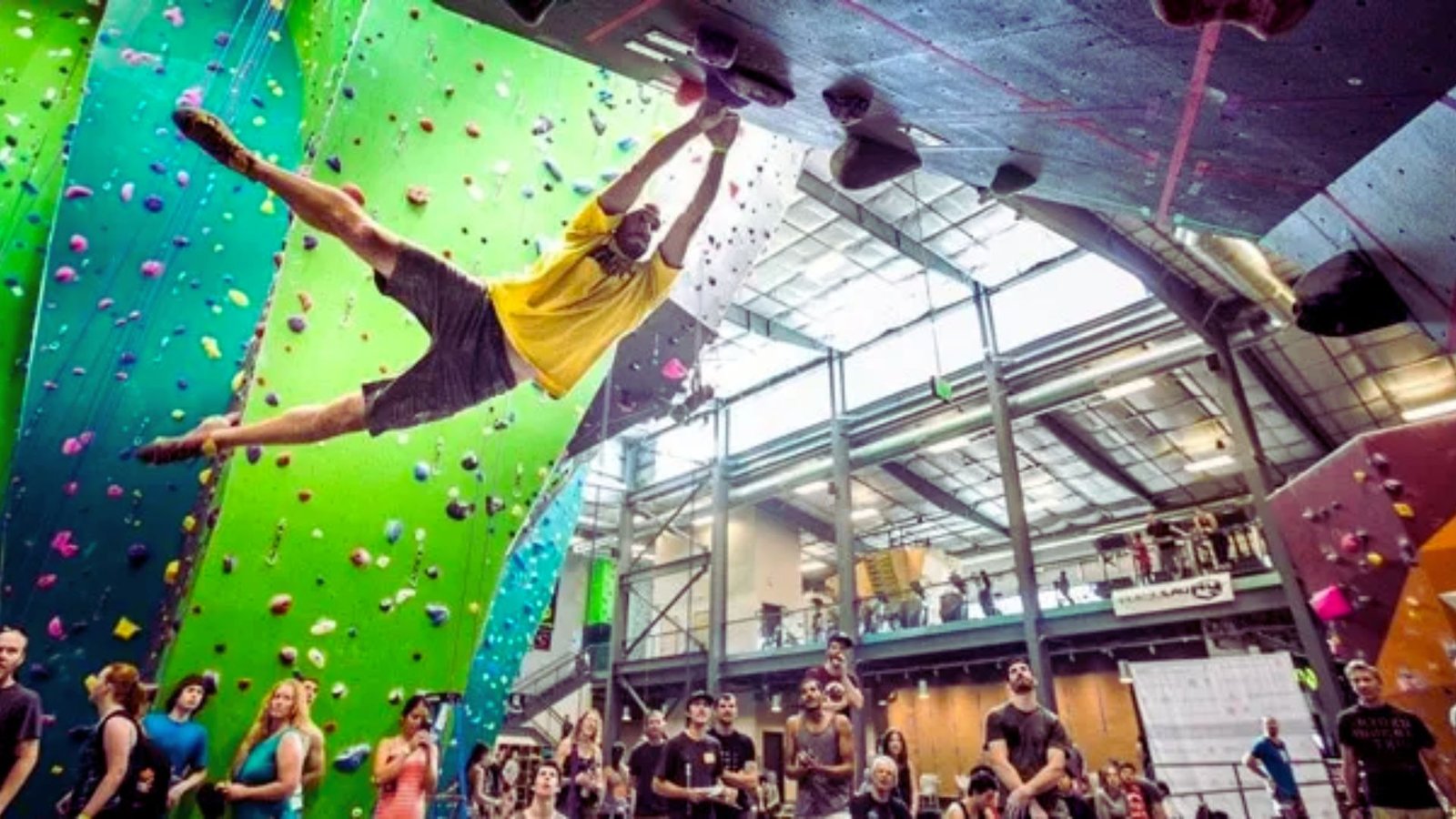 A man ascends a rock wall inside an indoor climbing gym, focused on his next handhold.