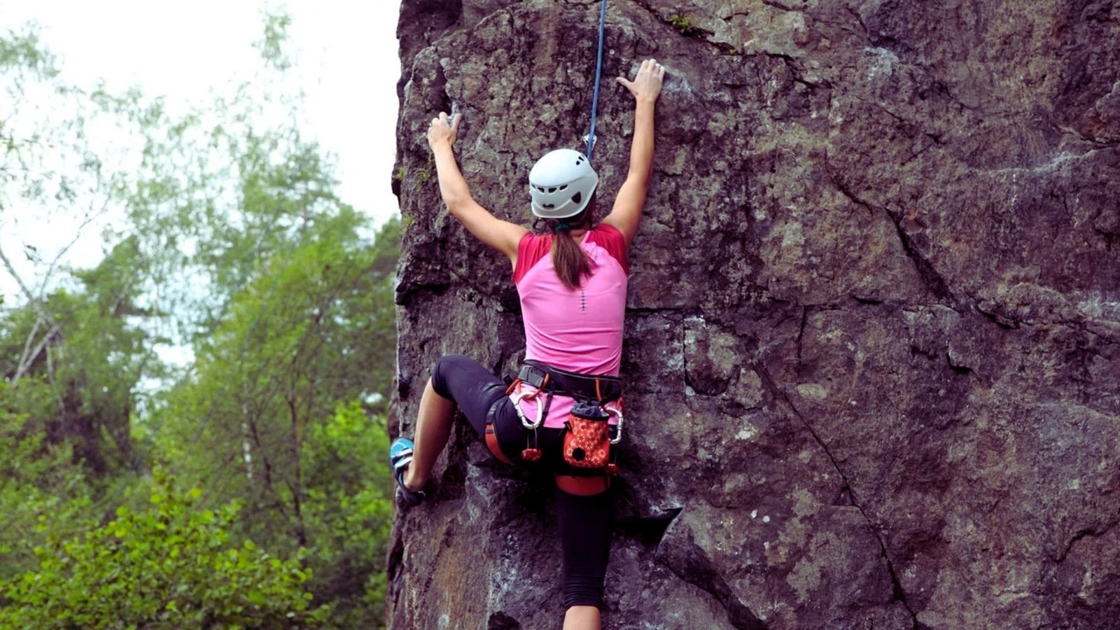 A woman wearing a helmet climbs a rock, demonstrating her skill and determination in outdoor climbing.