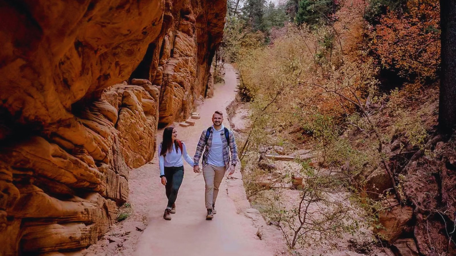 A couple walking hand in hand through a stunning canyon in Zion National Park, surrounded by towering red rock formations.