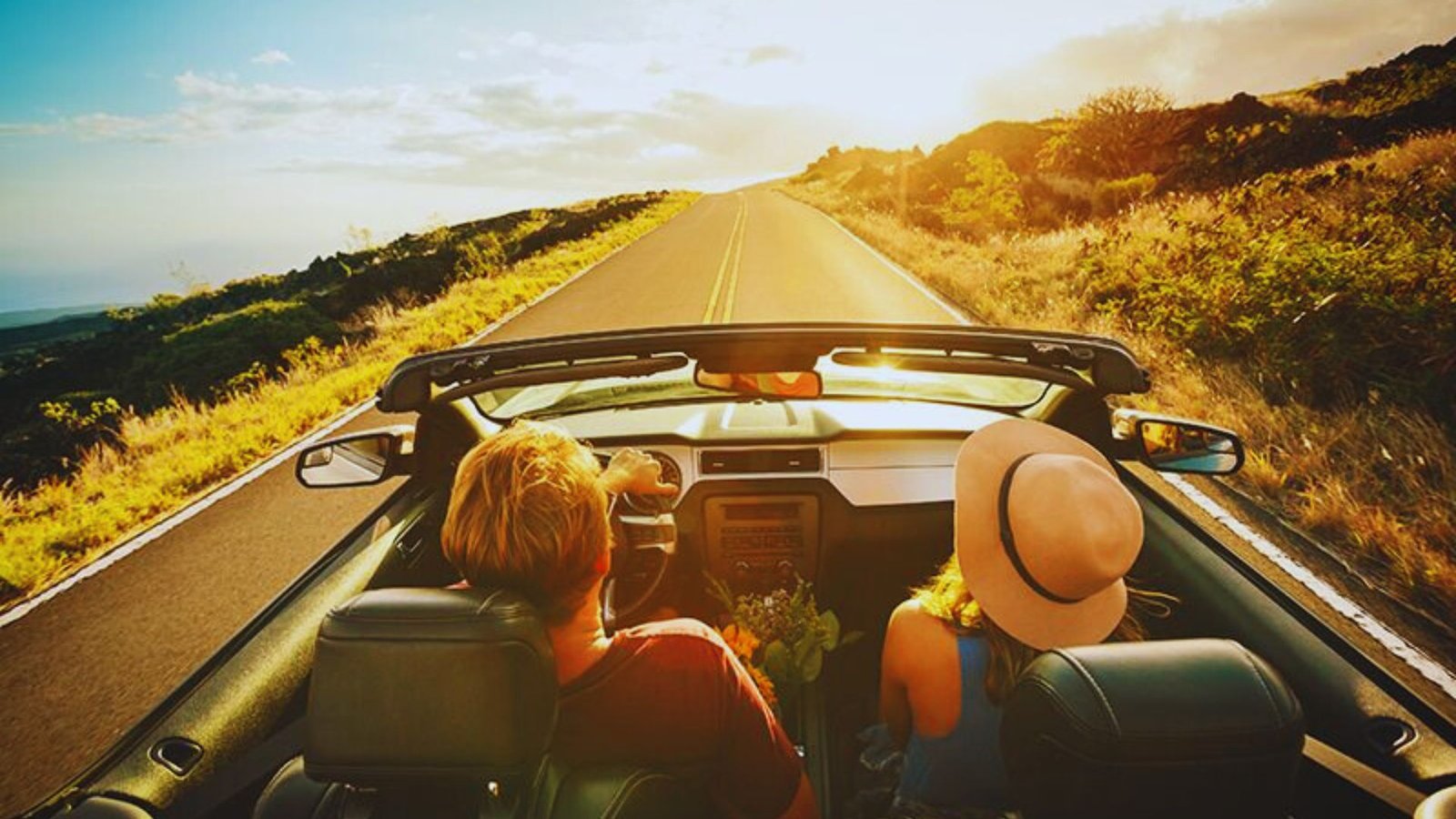 Two people enjoying a road trip in a convertible car, driving along a scenic road