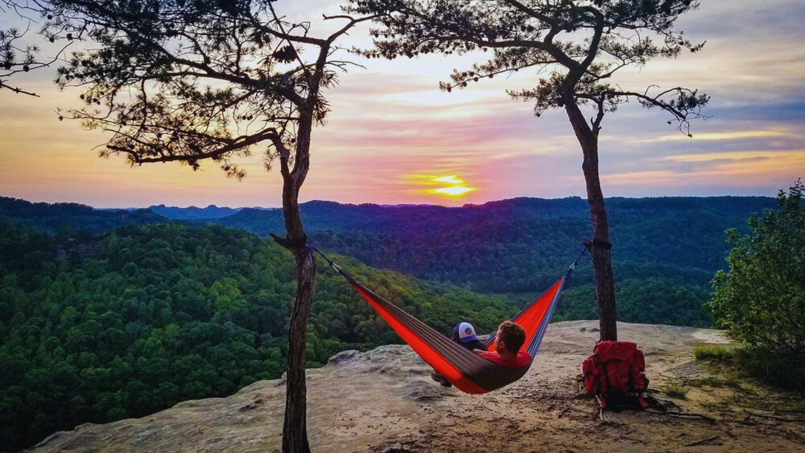 A person relaxing in a hammock on a mountain top, surrounded by scenic views of peaks and blue sky.