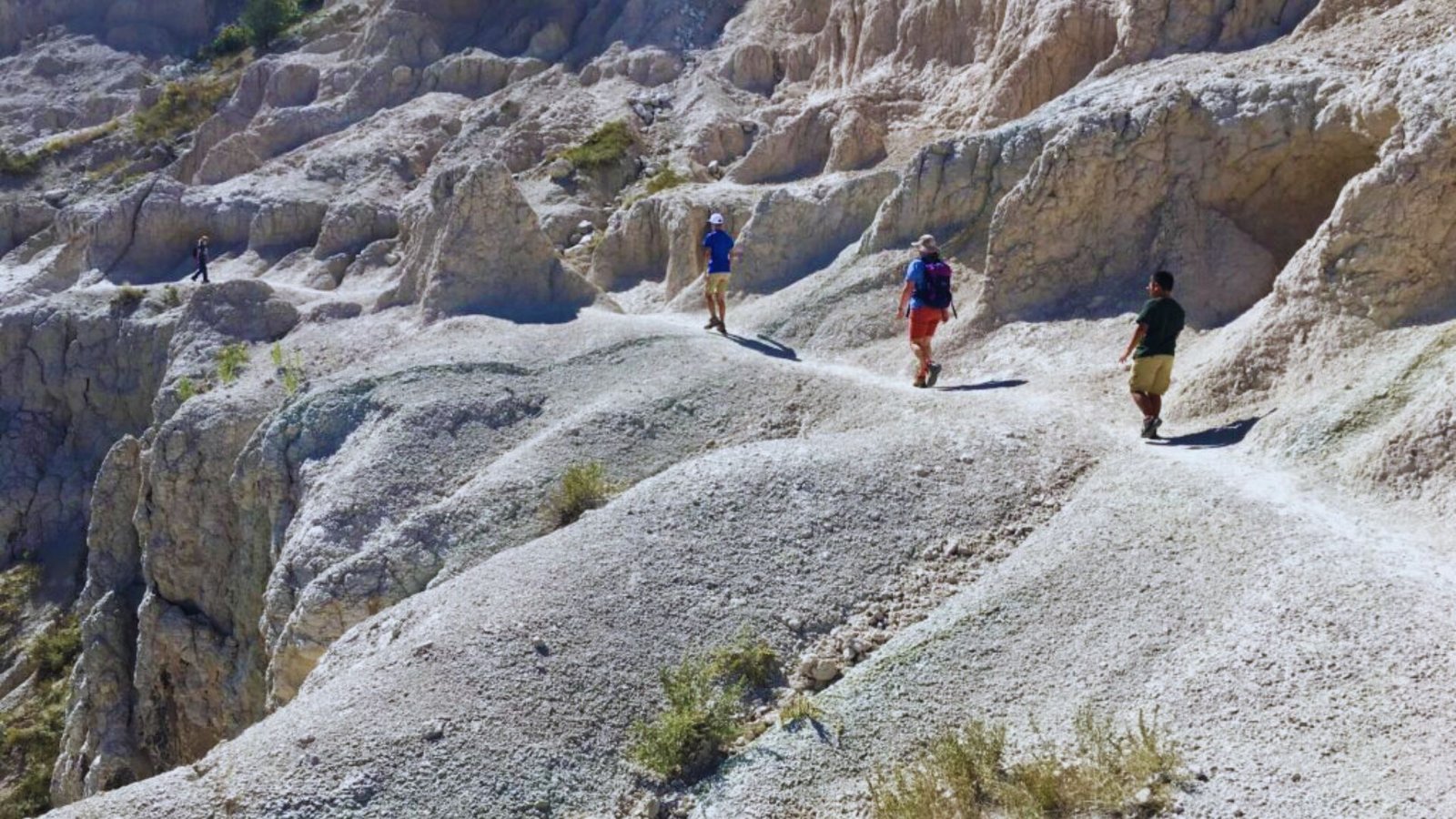 Three individuals walking along a winding path through the rugged terrain of the badlands.