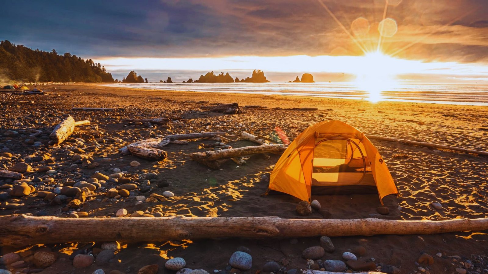  A tent is pitched on Shi Shi Beach, silhouetted against a vibrant sunset sky.
