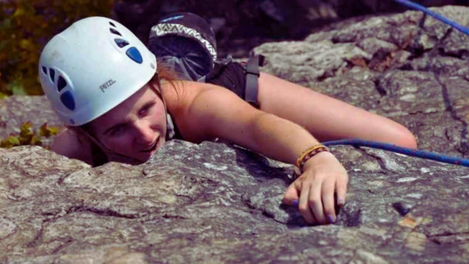 A woman wearing a helmet climbs a rocky surface, demonstrating her skill and focus in outdoor rock climbing.