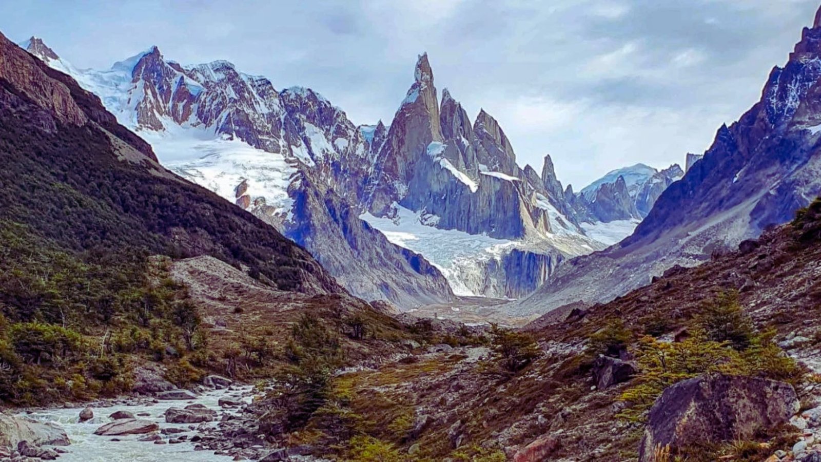 Majestic mountains of Patagonia rise against a clear blue sky, showcasing rugged peaks and lush green valleys.