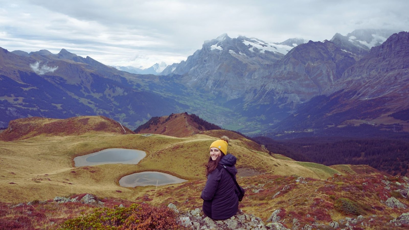  A woman atop a mountain gazes at a tranquil lake nestled in the valley below.