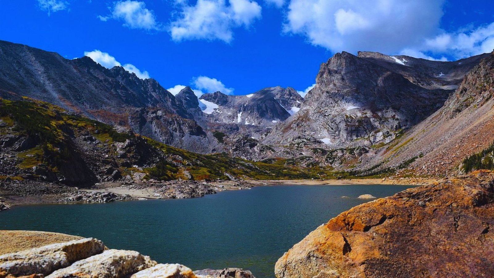 A serene lake nestled among towering mountains and rugged rocks under a clear blue sky.