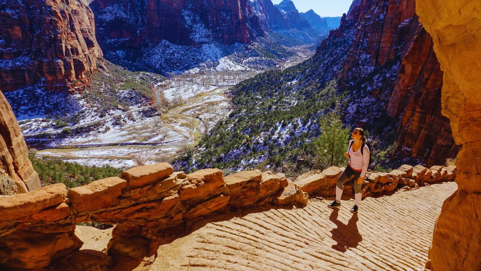 A person walking along a winding path surrounded by mountains under a clear blue sky.