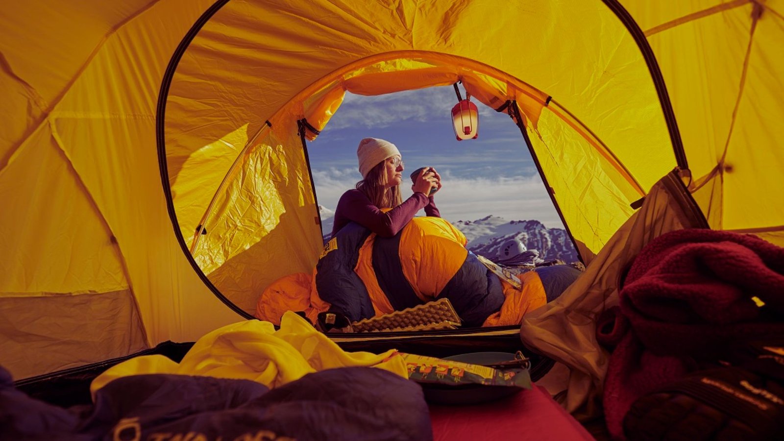 Inside a tent, a woman enjoys a breathtaking view of the mountains in the background.