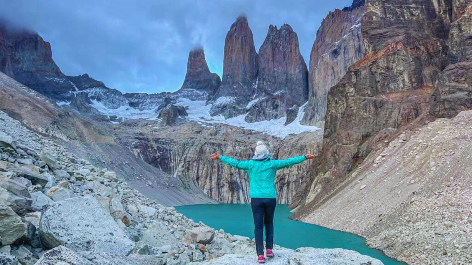A woman stands on a rock, gazing out over a serene lake surrounded by trees and mountains in the background.